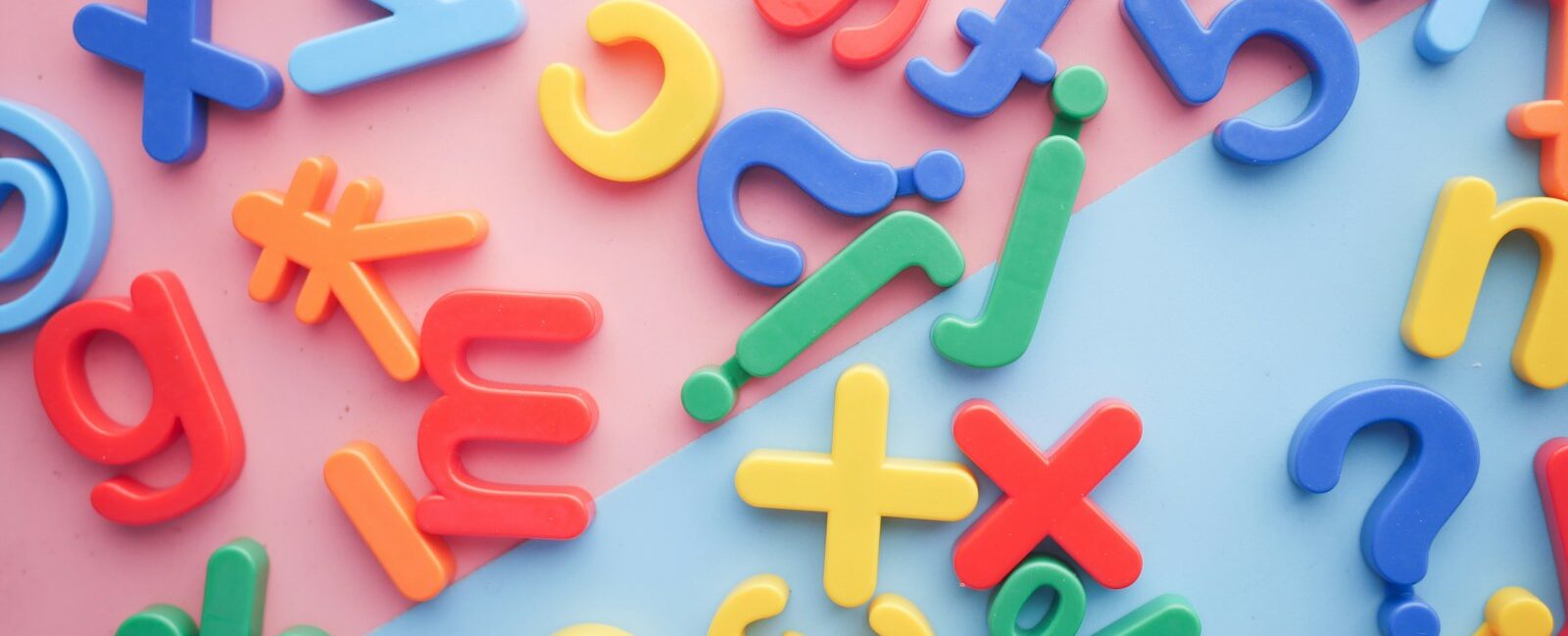 a scattered pile of plastic letters, numbers, and symbols on a pink and blue background that represent the challenges of language learning