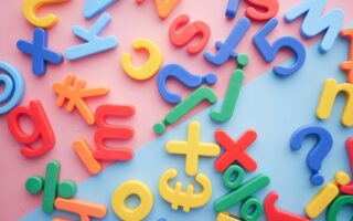 a scattered pile of plastic letters, numbers, and symbols on a pink and blue background that represent the challenges of language learning