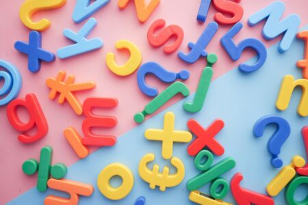 a scattered pile of plastic letters, numbers, and symbols on a pink and blue background that represent the challenges of language learning