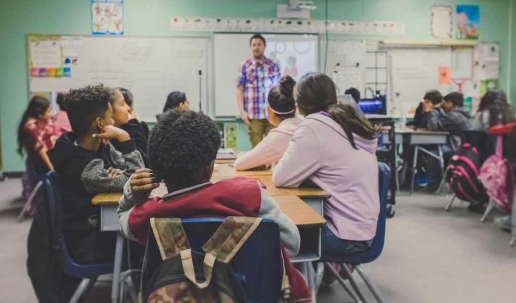 A classroom with children sitting on chairs while a male teacher is teaching