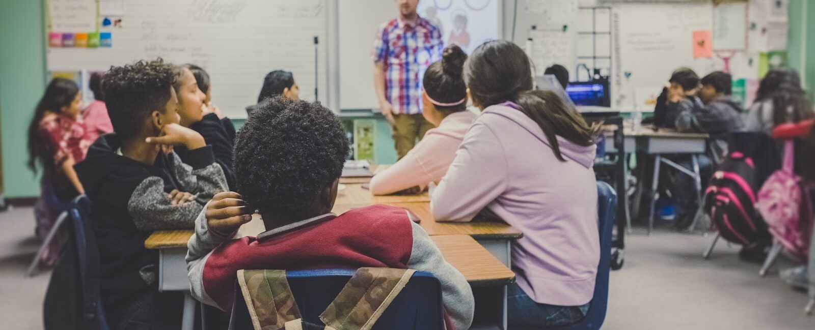 A classroom with children sitting on chairs while a male teacher is teaching