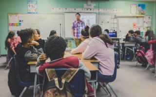 A classroom with children sitting on chairs while a male teacher is teaching