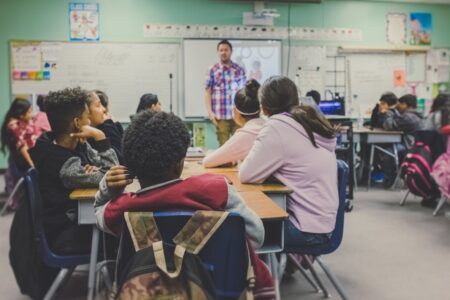 A classroom with children sitting on chairs while a male teacher is teaching