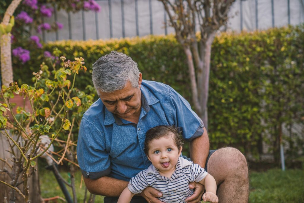 A grandfather in blue button up shirt carrying baby in black and white stripe shirt